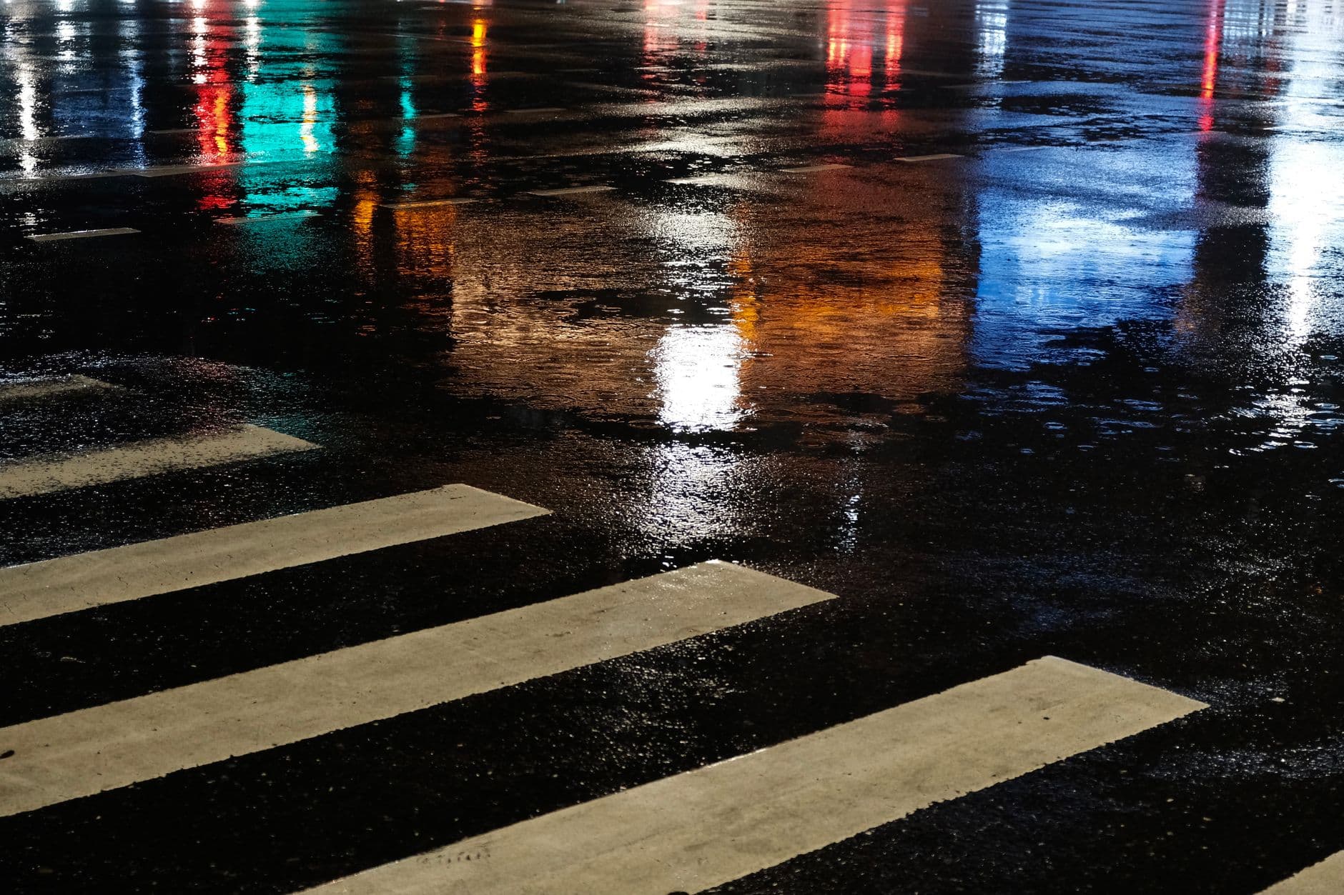 Passage piéton mouillé la nuit, reflets de lumières sur la chaussée