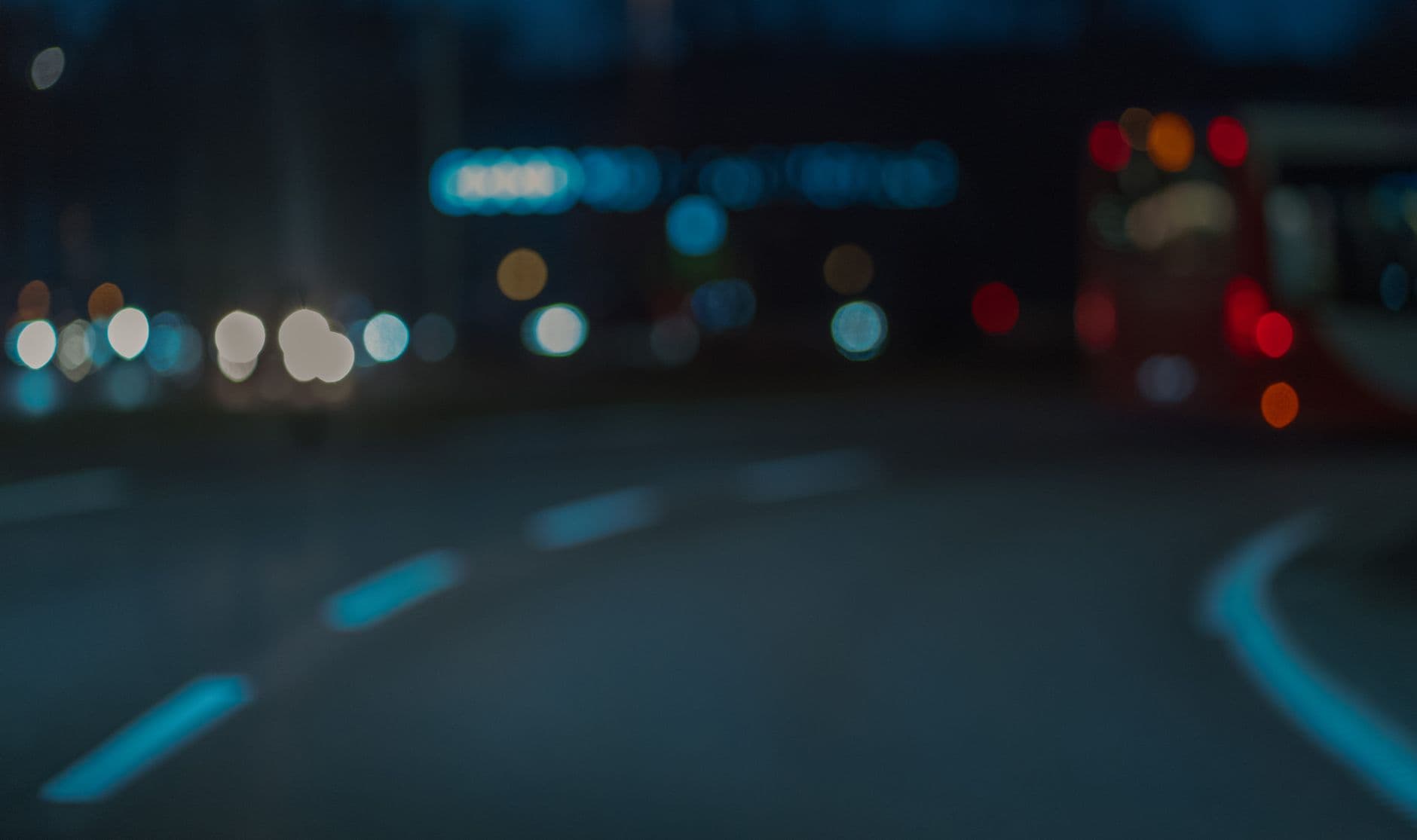 Route de nuit aux marquages blancs, lumières floutées au loin